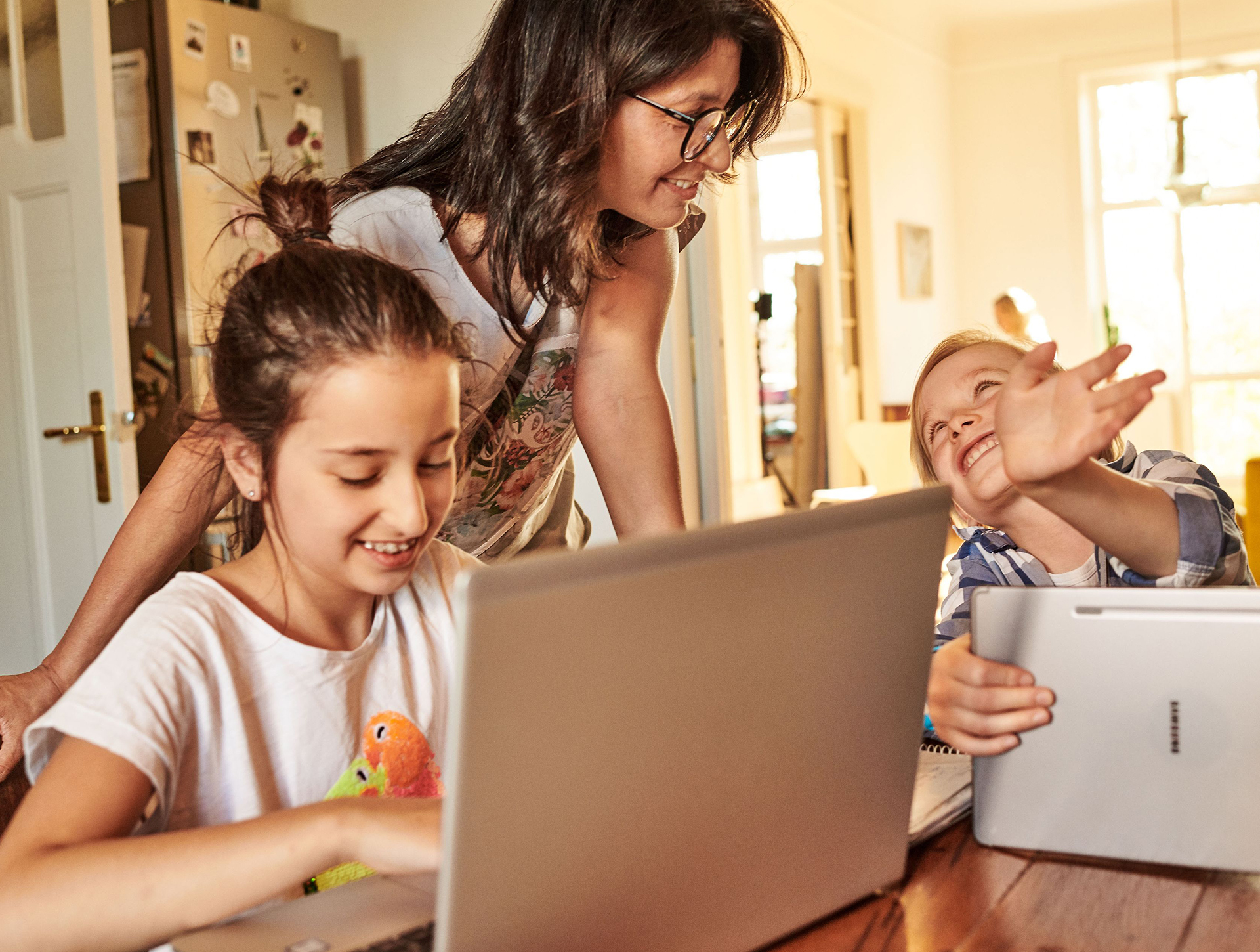 Dwie dziewczynki i mama korzystają z laptopa i tableta